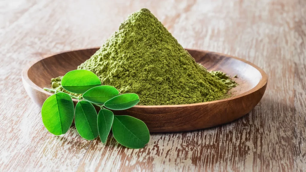 Moringa powder heaped in a wooden bowl with fresh moringa leaves