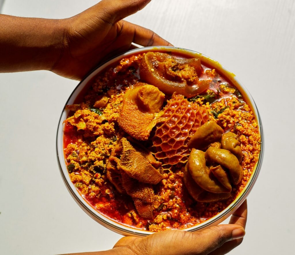 Hands holding a bowl of egusi soup with assorted meats
